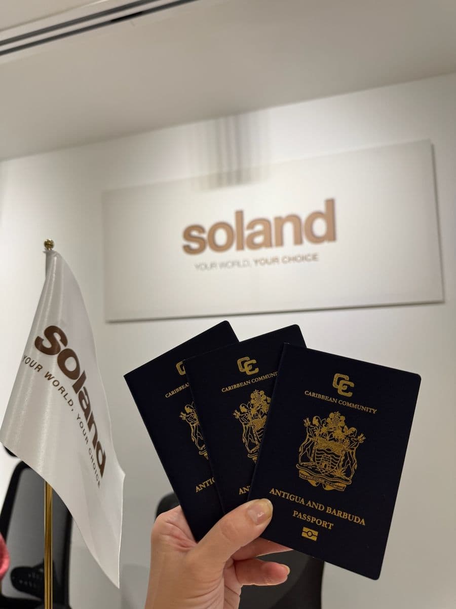 Three Antigua and Barbuda passports fanned out beside the Soland flag